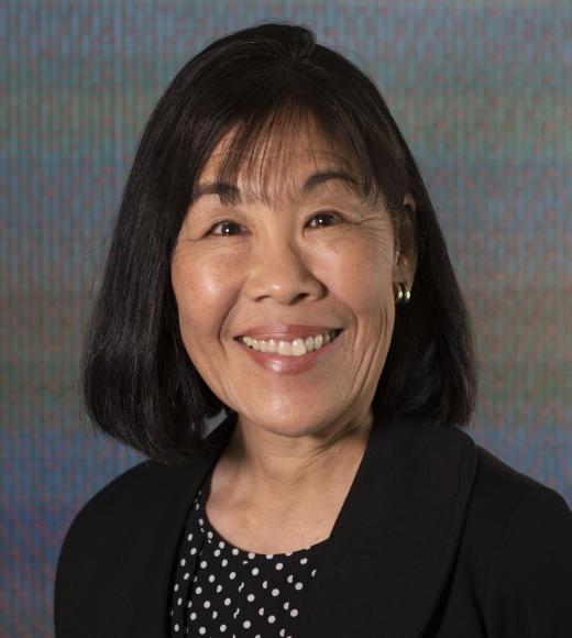 Professional headshot of an asian woman with black top with white dots and black jacket. This is Maureen Brodie