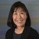 Professional headshot of an asian woman with black top with white dots and black jacket. This is Maureen Brodie